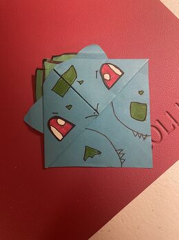 A green Bulbasaur-shaped origami pagekeeper resting on a book